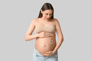 Poster - Young pregnant woman with heart made of cream on her belly against grey background