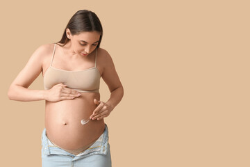 Wall Mural - Young pregnant woman with cream against stretch marks on beige background