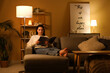 © Pixel-Shot - Young woman reading magazine and resting on cozy sofa in living room at night