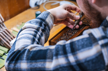 Wall Mural - man artisan carpenter carves pattern on wooden casket with a chisel in workshop in Tashkent in Uzbekistan