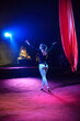 © Michael Rekochinsky - Professional aerial straps silks woman gymnast circus performance at red arena with dark background backlit with colored concert lights, performing gymnastic element