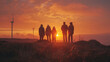 © Nano Photos - A group of five people stand together on a hill, watching a beautiful sunset with wind turbines in the background.