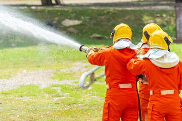 Wall Mural - Firefighter teamwork in fire suit on rescue duty using water from hose extinguishing fighting with big crackle fire flames inside burning premises. Fireman spraying high pressure water fight a fire.