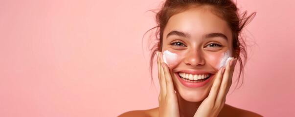 Wall Mural - Happy smiling young woman with perfect skin puts a moisturizing cream on her face. Girl using skincare product on facial skin. Natural beauty and cosmetic concept. Banner with copy space