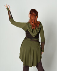Wall Mural - portrait of beautiful red haired female model, wearing green and brown medieval fantasy costume with tunic and armour. Standing  pose facing away backwards , isolated on white studio background.