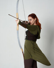 Wall Mural - close up portrait of red haired female model wearing green medieval fantasy costume, leather armour.
Holding archery bow and arrow weapon, standing action pose isolated on white studio background.