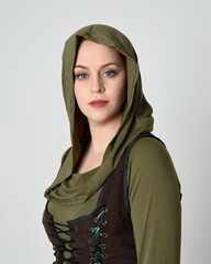 Wall Mural - Close up portrait of beautiful red haired female model, wearing green and brown medieval fantasy costume with hooded shirt and brown tunic. isolated on white studio background.