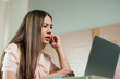 © Ekkasit A Siam - Asian woman working on laptop with concerned expression. Long hair, casual attire, modern home office setting. Intense focus on screen, indoor environment, beige and white decor, natural lighting
