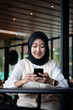 © Stora Space - beautiful indonesian woman wearing a black hijab smiling and holding a phone