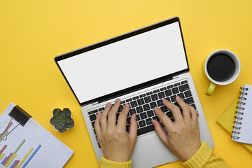 Wall Mural - Above view unrecognizable woman hands typing on laptop keyboard over yellow background