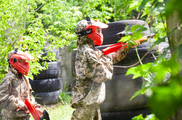 Fastiv, Kyiv region, Ukraine 05.31.2024,People wearing  helmets and camouflage are playing paintball, there are many obstacles and green trees with leaves around.People are focused on playing in sunny