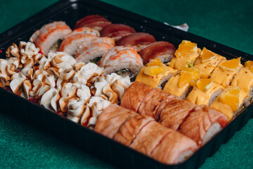 Big tasty set of sushi with fish, avocado, shrimp and cheese on a green background