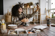 © sofiko14 - Female potter recording a pottery tutorial on her smartphone while working on a piece in her studio. Cozy, creative workspace with shelves and supplies in the background.