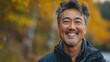 © Антон Сальников - An Asian-American man in his 50s exudes happiness and a sense of being truly alive in a beautiful natural park near a lake. He has a genuine smile on his face.