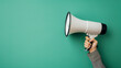 © AndreyFrol - Female hand with a plaid coat with a white hand-held loudspeaker on a green background. Organization and leadership during public events and holidays.