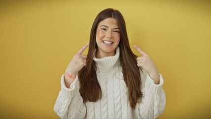 Sticker - Joyful young hispanic woman in sweater, standing over yellow isolated background, cheerfully points to perfect, white teeth, highlighting dental health with a radiant smile