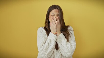 Wall Mural - Laughing out loud, young, beautiful hispanic woman in sweater, covering mouth in embarrassed gossip scandal, standing isolated over yellow background