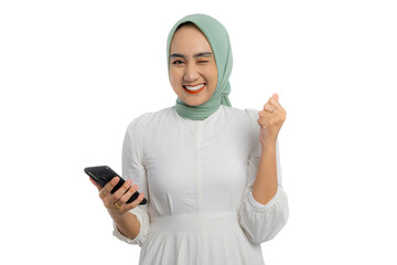 Wall Mural - Excited young Asian woman in green hijab and white blouse using smartphone, gesturing yes with clenched fist, celebrating great news isolated on white background