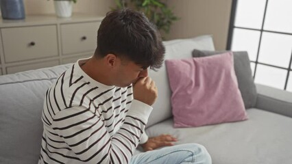 Sticker - Young hispanic man coughing while sitting on a sofa in a cozy living room setting indoors, highlighting a moment of discomfort due to illness.