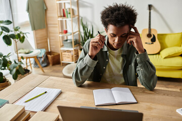 Wall Mural - A young African American man sits at a desk with a laptop.