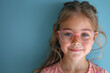 © Helena GARCIA - niña sonriente de pelo rubio con gafas graduadas de pasta en color rosa, sobre fondo azul claro