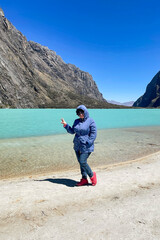 Wall Mural - A woman standing on a beach with a blue lake in the background. Llanganuco lagoon, Peru