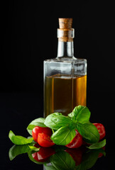 Canvas Print - Bottle of olive oil and tomatoes with basil on a black background.