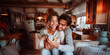 © Pavel Lysenko - A young couple sits close together on a couch in a rustic kitchen, the woman holding a mug and smiling warmly at the camera. The man holds her close, his arm around her shoulders