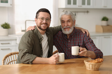 Wall Mural - Happy son and his dad with cups at wooden table in kitchen