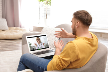 Wall Mural - Online medical consultation. Man having video chat with doctor via laptop at home