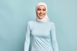 © CogniLens - Portrait of a cheerful woman in her 30s showing off a lightweight base layer isolated in pastel blue background