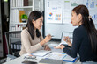 © Wasana - Two women are sitting at a desk with a whiteboard behind them