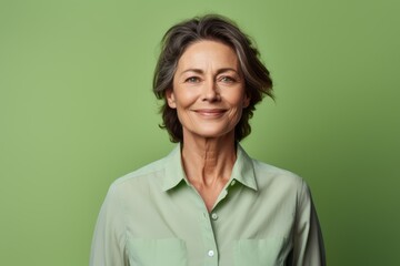 Portrait of a glad woman in her 50s wearing a simple cotton shirt isolated in pastel green background