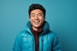 © CogniLens - Portrait of a grinning asian man in his 30s sporting a quilted insulated jacket isolated on soft blue background