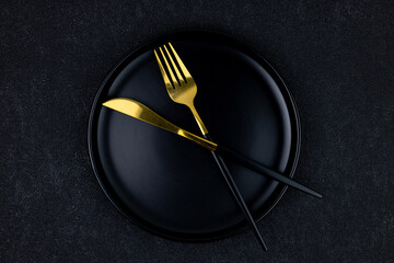 Black plate with fork and knife on black concrete background top view