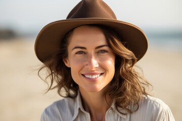 Wall Mural - Portrait of a smiling woman in her 30s wearing a rugged cowboy hat while standing against sandy beach background