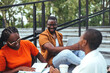 © Dragana Gordic - A group of black university students engages in a lively discussion on campus stairs, with books and a laptop, dressed in casual attire.