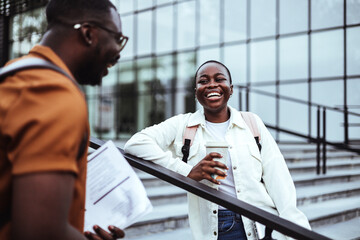 Wall Mural - A joyful male and female student engage in a friendly conversation on university stairways, with books in hand, reflecting a casual educational setting.