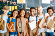 © Jane_S - Diverse group of school children smiling and holding books in a classroom.