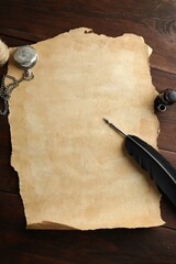 Sheet of old parchment paper, black feather, inkwell and pocket chain clock on wooden table, flat lay