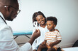 © Dragana Gordic - A little boy looks attentively at a male doctor while sitting on his mother's lap, both in a medical office for a check-up, displaying trust and care in a healthcare setting.