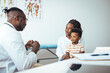 © Dragana Gordic - A young black boy sits attentively with his mother during a consultation as a doctor in a white coat takes notes, indicative of pediatric health care services.