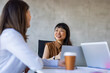 © Dragana Gordic - An Asian and a Caucasian businesswoman engage in a collaborative discussion at a modern office, laptops and coffee at hand, highlighting teamwork and professionalism in a corporate setting.