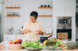 © NewSaetiew - A woman is cooking in a kitchen with a lot of fresh vegetables and fruits