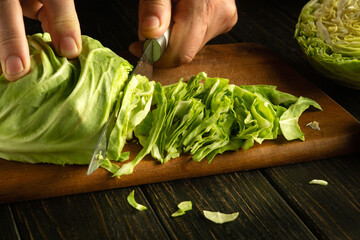 Wall Mural - Preparing a salad from fresh cabbage. The hand of a cook with a knife cuts cabbage on a kitchen board for preparing a vegetarian dish.