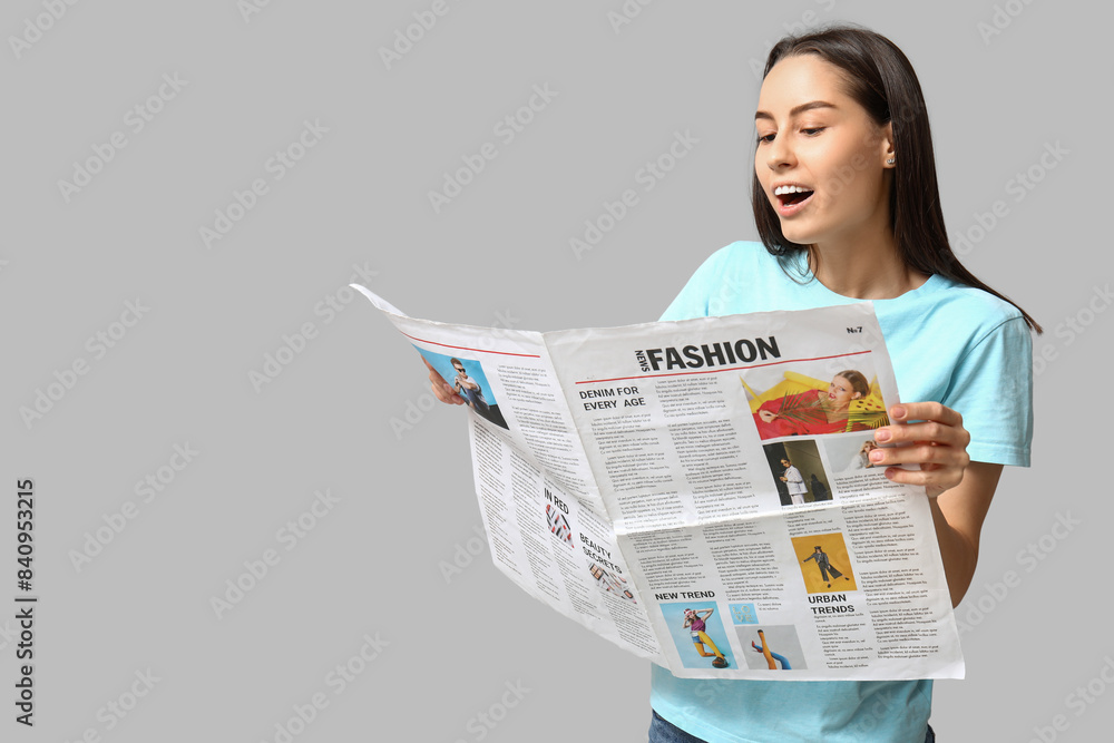 Beautiful young woman with newspaper on grey background