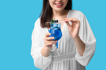 Wall Mural - Young woman holding glass of tasty cocktail with blueberry on blue background