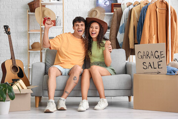 Canvas Print - Happy young couple sitting on sofa in room of unwanted stuff. Garage Sale