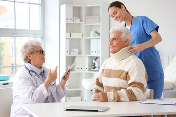 Wall Mural - Senior doctor and nurse putting cervical collar on mature man in clinic