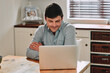 © peopleimages.com - Laptop, smile and businessman in kitchen reading email or online communication for career. Technology, happy and male hr freelancer work on startup company policy review with computer at home.